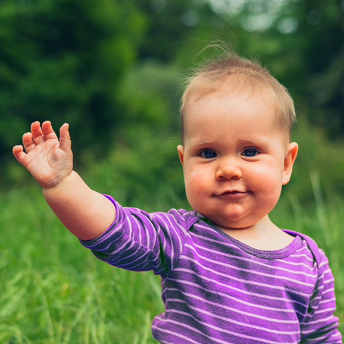 baby sitting in grass waving with arm in the air